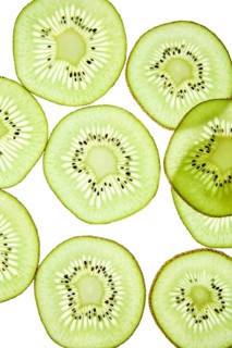 Close up of fresh kiwi slices arranged against a light background. The vibrant green fruit exhibits