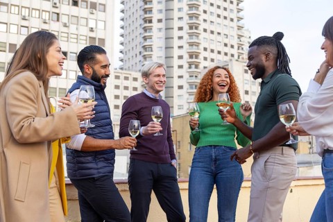A lively group of friends celebrate on a rooftop, holding glasses of white wine They share laughter