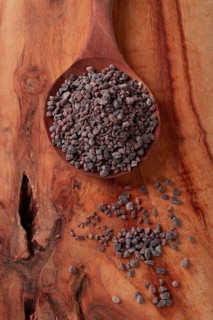 Crystals of black salt, on a wooden spoon, laid out on a wooden surface, top view