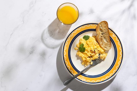 A vibrant breakfast scene featuring creamy scrambled eggs garnished with herbs, toast, and a glass