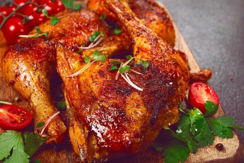 Grilled fried chicken legs, served with fresh cherry tomatoes, and herbs, on a wooden chopping