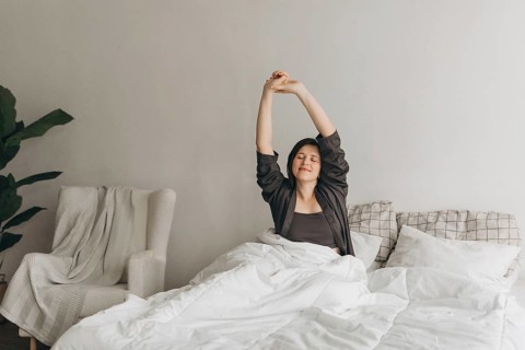 A woman stretches in bed, enjoying a morning routine promoting energy and wellness. The serene