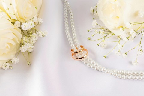 Wedding rings placed gracefully on a string of pearls, surrounded by white roses and delicate
