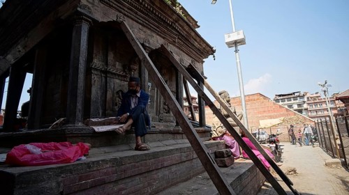 Man sits in front of a temple secured by support beams on Durbarsquare in Kathmandu and reads a