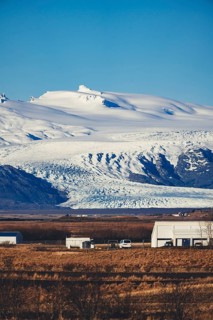 Distant view of a glacier from the Stokksnes area in Iceland, with small rural buildings and golden