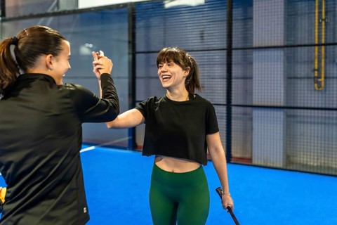 Two young women high fiving on an indoor pickleball court, smiling and celebrating teamwork,