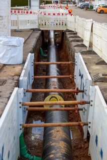 Large district heating pipeline runs through a construction site trench with stabilising wooden