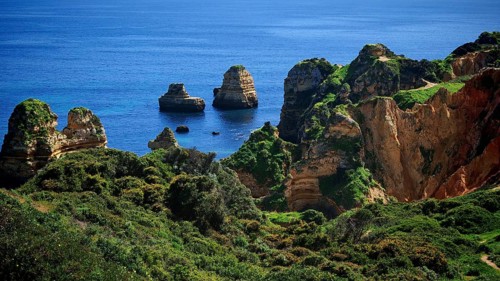 Impressive rock formations in the blue sea and lush green vegetation, Praia do Camilo, Lagos,