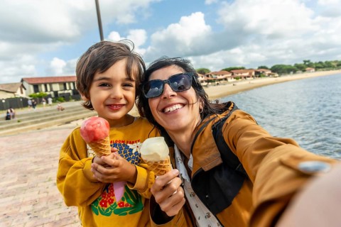 Mother and son smiling for a seaside selfie, enjoying ice cream cones during a sunny summer holiday