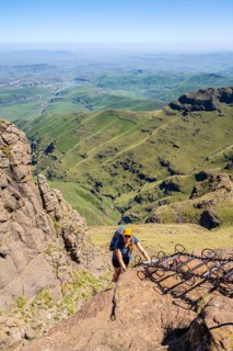 Young female hiker climbs over dangerous ladders, mountains and cliffs of the Drakensberg