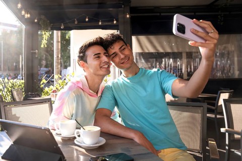 A cheerful gay couple enjoys sunny moments, taking a selfie together at an outdoor cafe. Relaxed