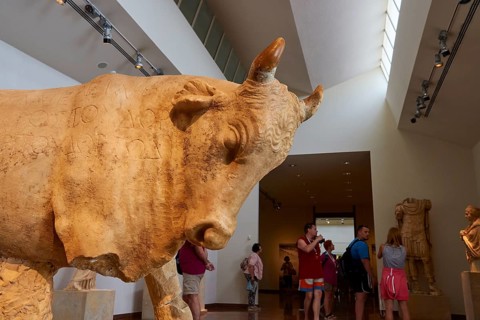 Large bull statue in a museum with visitors in the background, Olympia Archaeological Museum,