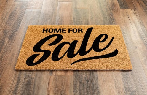 Home For Sale Welcome Mat On A Wood Floor Background