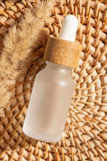 A frosted cosmetic with a wooden cap is placed on a woven basket. The natural texture and sunlight