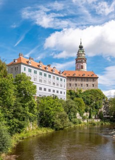 View of the Ceský Krumlov Castle with tower, colorful facade buildings, Vltava River, and greenery