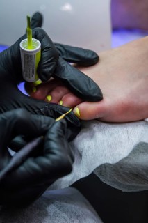 Vertical closeup of toenail polish being applied during a professional pedicure, with gloved hands