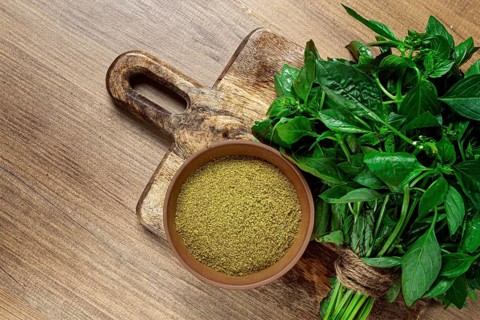 Ground green basil, in a ceramic bowl, with a bouquet of fresh green basil, on the table, top view,