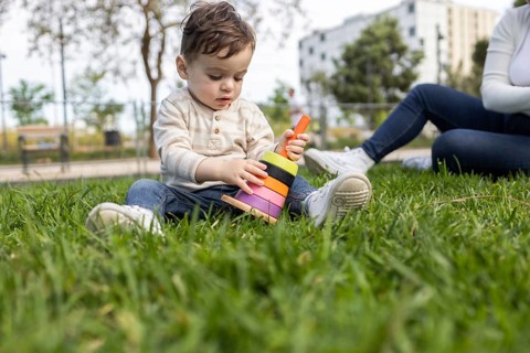 A baby joyfully plays with colorful toys while his mother watches attentively. They are enjoying a