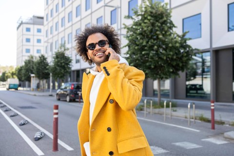 A businessman with afro hair wearing a stylish yellow coat and sunglasses, happily talking on the