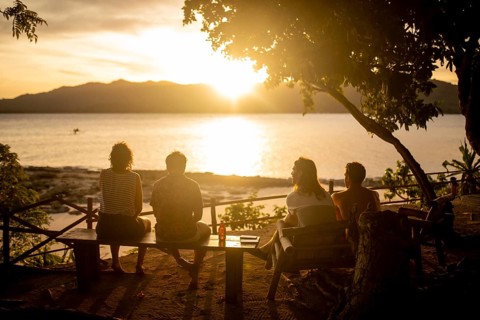 Back view of unrecognizable friends sitting together on a bench, enjoying a breathtaking sunset