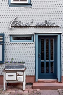 Residential house clad with wooden shingles, old oven for decoration in front of design hotel Die