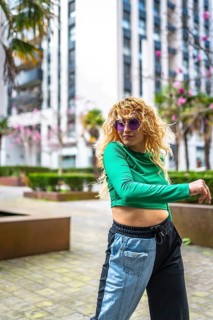 Young woman with curly hair and sunglasses enjoying dance in a modern cityscape. Vibrant energy and