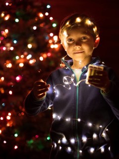 Cute boy playing with Christmas lights and Christmas tree in the background.