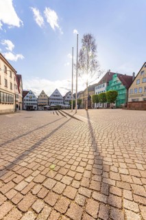 A wide, sunny square with a tree and surrounding houses makes for a peaceful impression, Weil der