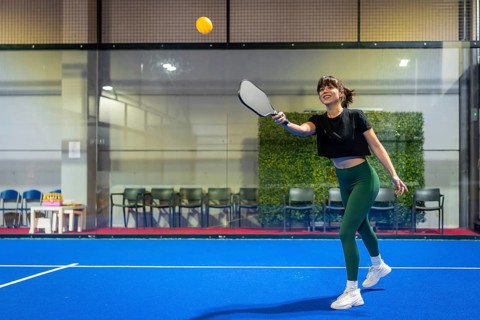 Woman playing pickleball on an indoor blue court, smiling while hitting the ball with her paddle,