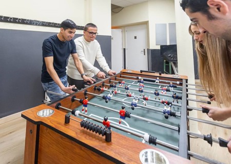 A diverse group takes part in a lively game of table football at a mental health leisure center,