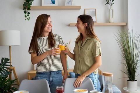 A lesbian couple shares a joyful moment at home, clinking glasses of orange juice Surrounded by