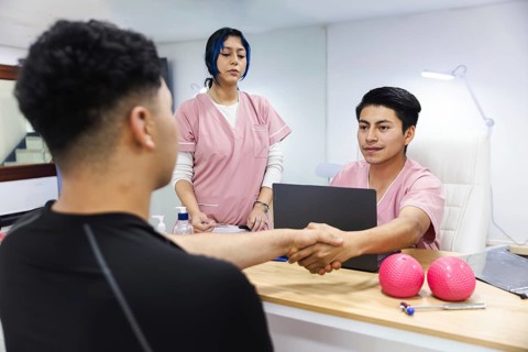 In an Ecuadorian physiotherapy clinic, a patient shakes hands with a smiling therapist. An