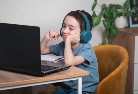 A young boy wearing headphones is focused on a laptop screen, participating in an online learning