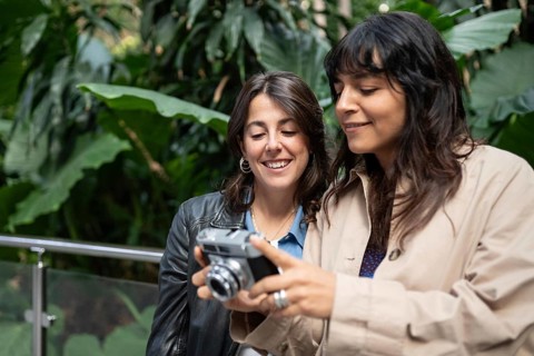 A multiethnic lesbian couple enjoys a joyful moment together, looking at a vintage camera. Dressed