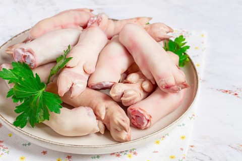 Pork trotters arranged on a plate with fresh parsley on a white background