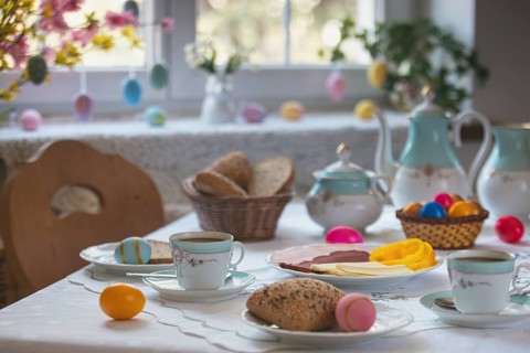 Breakfast table with Easter eggs, pastries and cold plate in front of decorated window