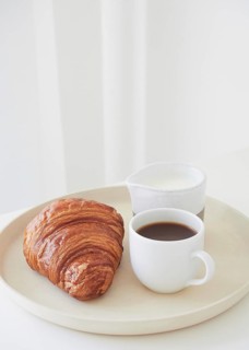 Minimalist monochromatic composition of simple breakfast: plate with croissant, coffee cup and milk