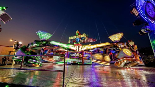 Lively funfair with fast-turning, illuminated carousel at night, carousel and the hustle and bustle