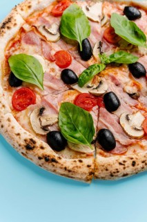 Top view of a freshly baked pizza topped with bacon, mushrooms, mozzarella cheese, black olives,