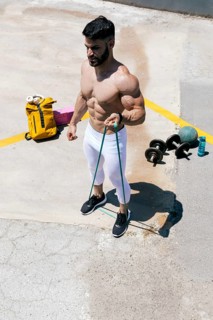 A muscular man exercises outdoors on a sunny day, using resistance bands. Fitness equipment,