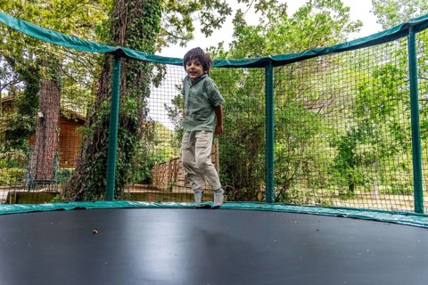 Young child experiencing joy and freedom while bouncing on an outdoor trampoline with a safety net,