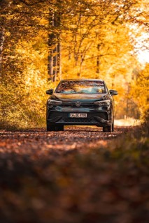 Car on an autumn path in the forest, immersed in golden leaves and sunlight, electric car VW ID5,