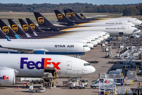 FedEx Express Boeing 777-FS2 cargo plane is unloaded, air freight container, behind cargo fleet of