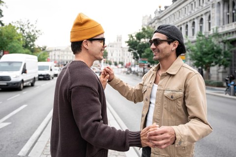 A gay couple shares a joyful moment on an urban street. They hold hands, smiling warmly at each