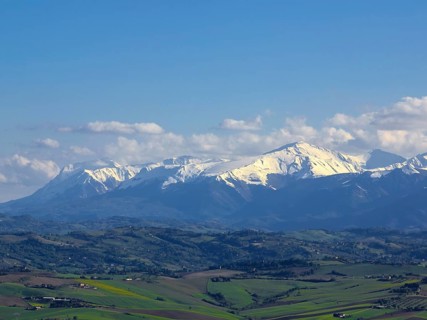 A breathtaking view of snow-capped mountains under a clear blue sky over lush green Italian