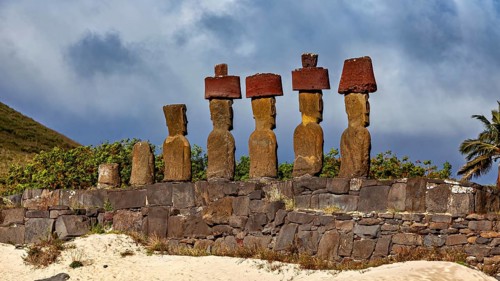 Row of Moai statues, cloudy sky and palm trees on Easter Island convey historic atmosphere, the
