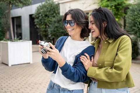 A joyful lesbian couple laughing while viewing photos on a camera. They are enjoying each other's