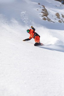 Snowboarder in bright orange gear skillfully carves down a snowy mountain slope. Captured in