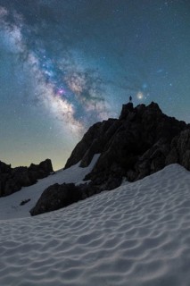 A lone figure stands on a snowy Icelandic peak beneath a stunning Milky Way sky The scene captures