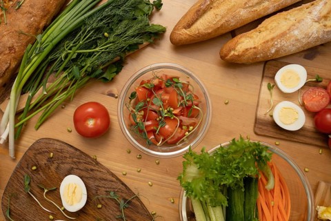A vibrant tabletop spread featuring crusty baguettes, fresh vegetables, hard-boiled eggs, and a